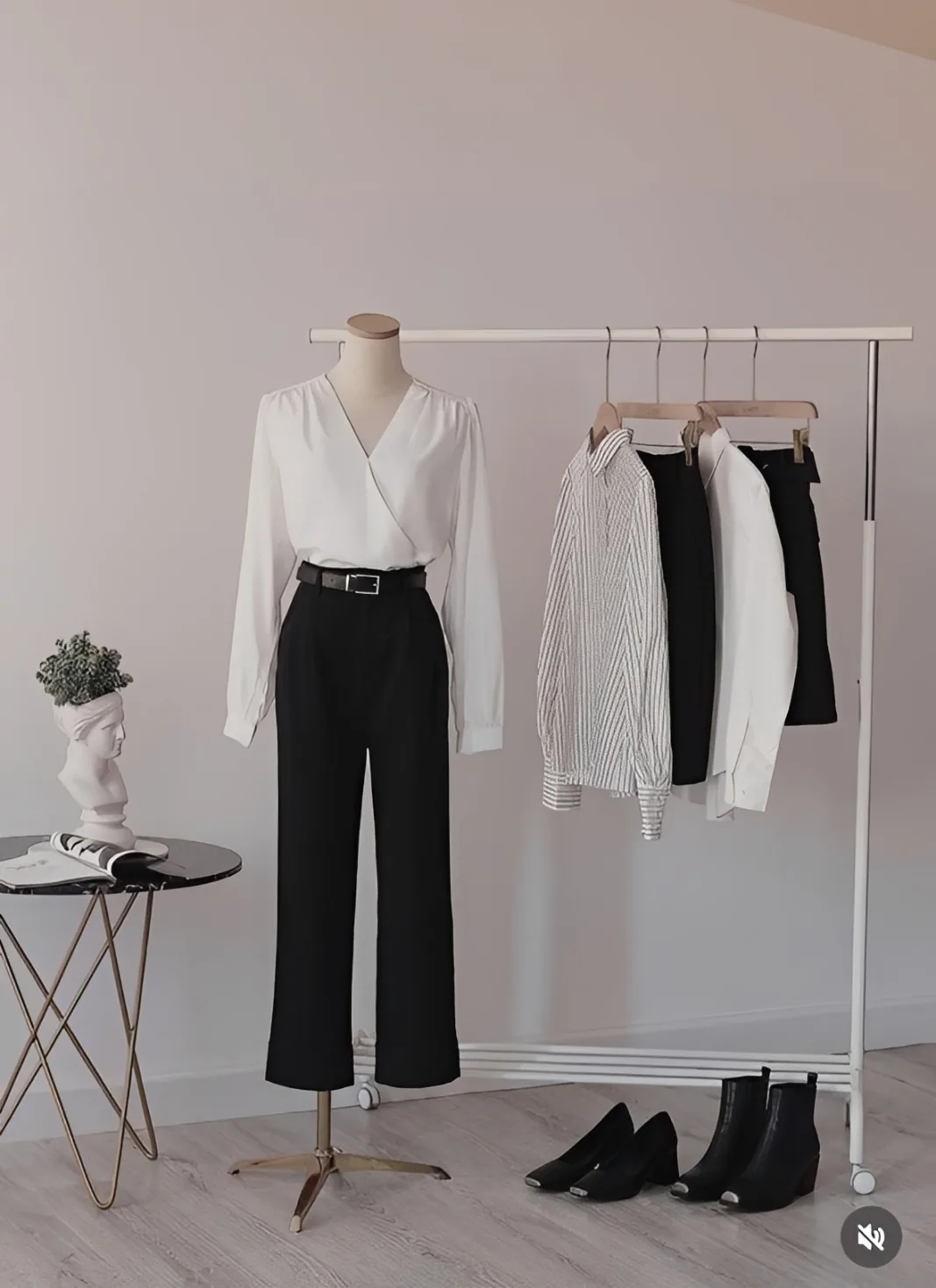 Maniquí con blusa blanca y pantalón negro junto a un perchero con prendas y botines.