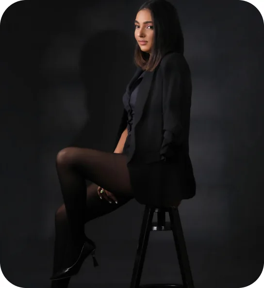 Karen Voguedo con blazer negro, sentada en un taburete sobre fondo oscuro.